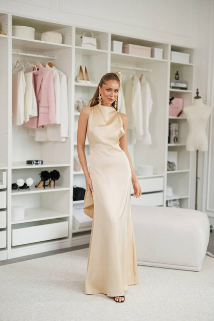 Woman in a long beige dress standing in a stylishly organized room with shelves and decor.