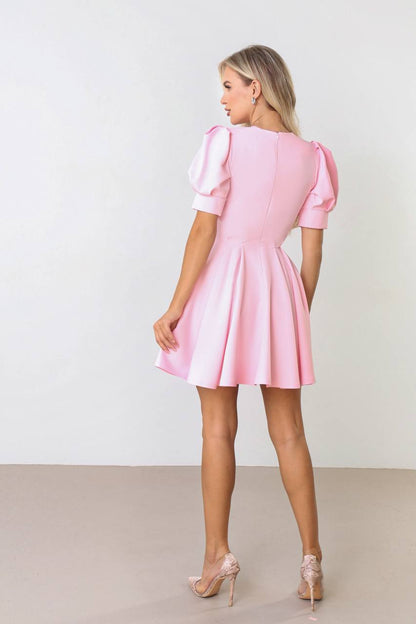 Woman wearing a pink dress with puff sleeves against a white background