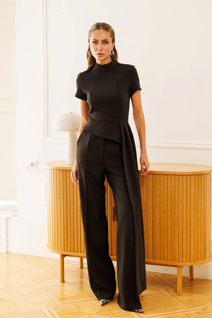 Woman in a black outfit standing in a room with wooden furniture.