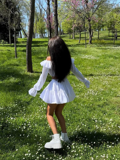 Person in a white outfit standing in a park with green grass and trees.