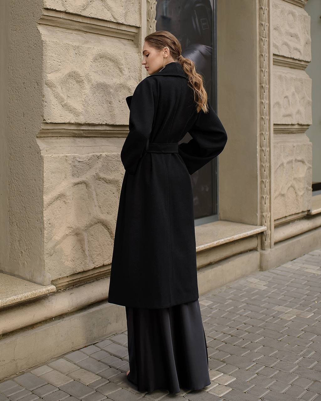Woman wearing a black coat standing in front of a building entrance.