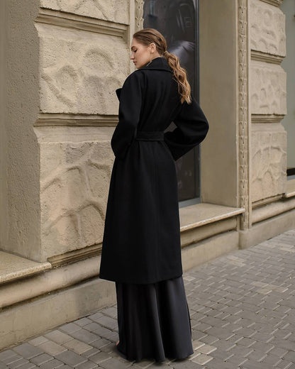 Woman wearing a black coat standing in front of a building entrance.