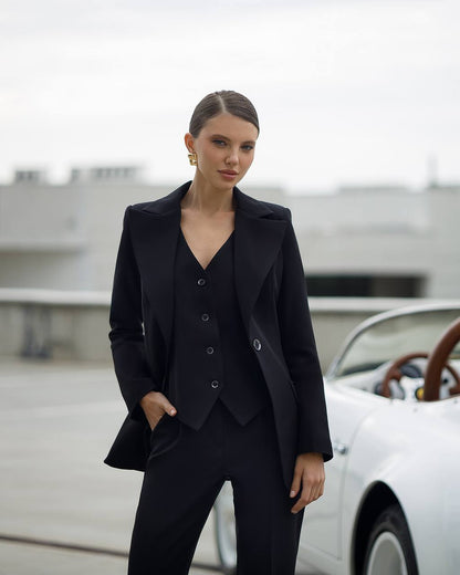 Woman in a black suit standing in front of a vintage car