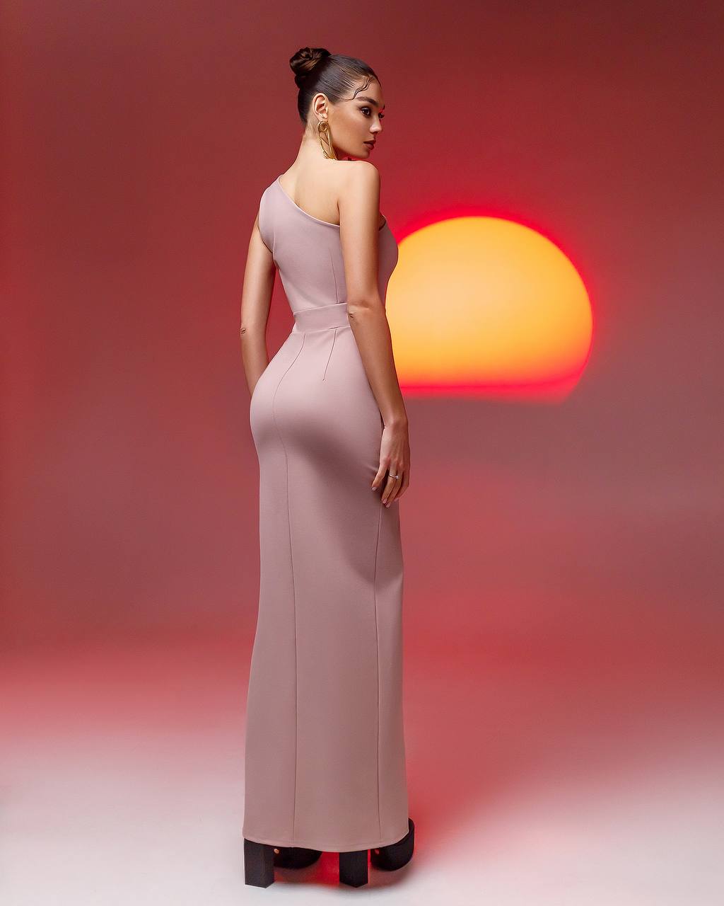 Woman in a long, elegant dress standing against a gradient background with a warm light.