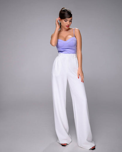 Woman wearing a purple top and white pants on a gray background