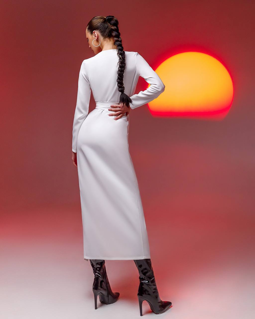 Woman in a white dress with black high-heeled boots standing against a red and orange gradient background.