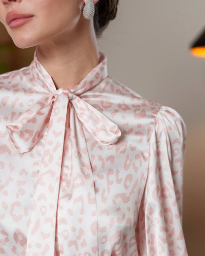 Close-up of a person wearing a pink leopard print blouse with a bow detail.
