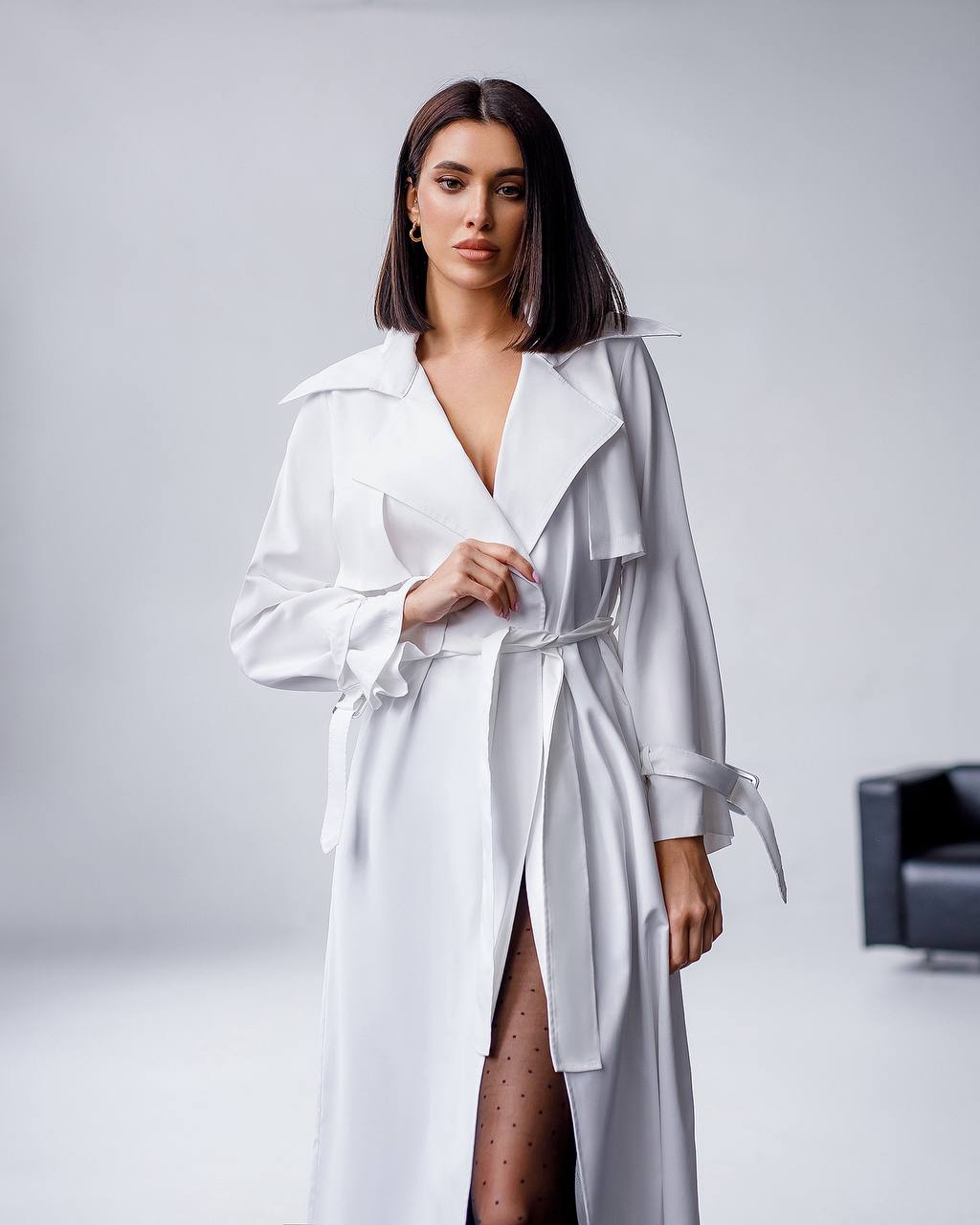 Woman wearing a white trench coat against a plain background