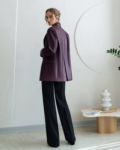 Woman in a purple coat and black pants standing in a modern interior setting.