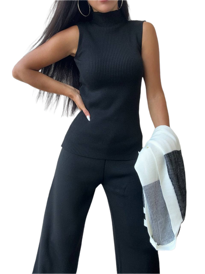 Woman wearing a black sleeveless top and pants holding a white jacket on a white background