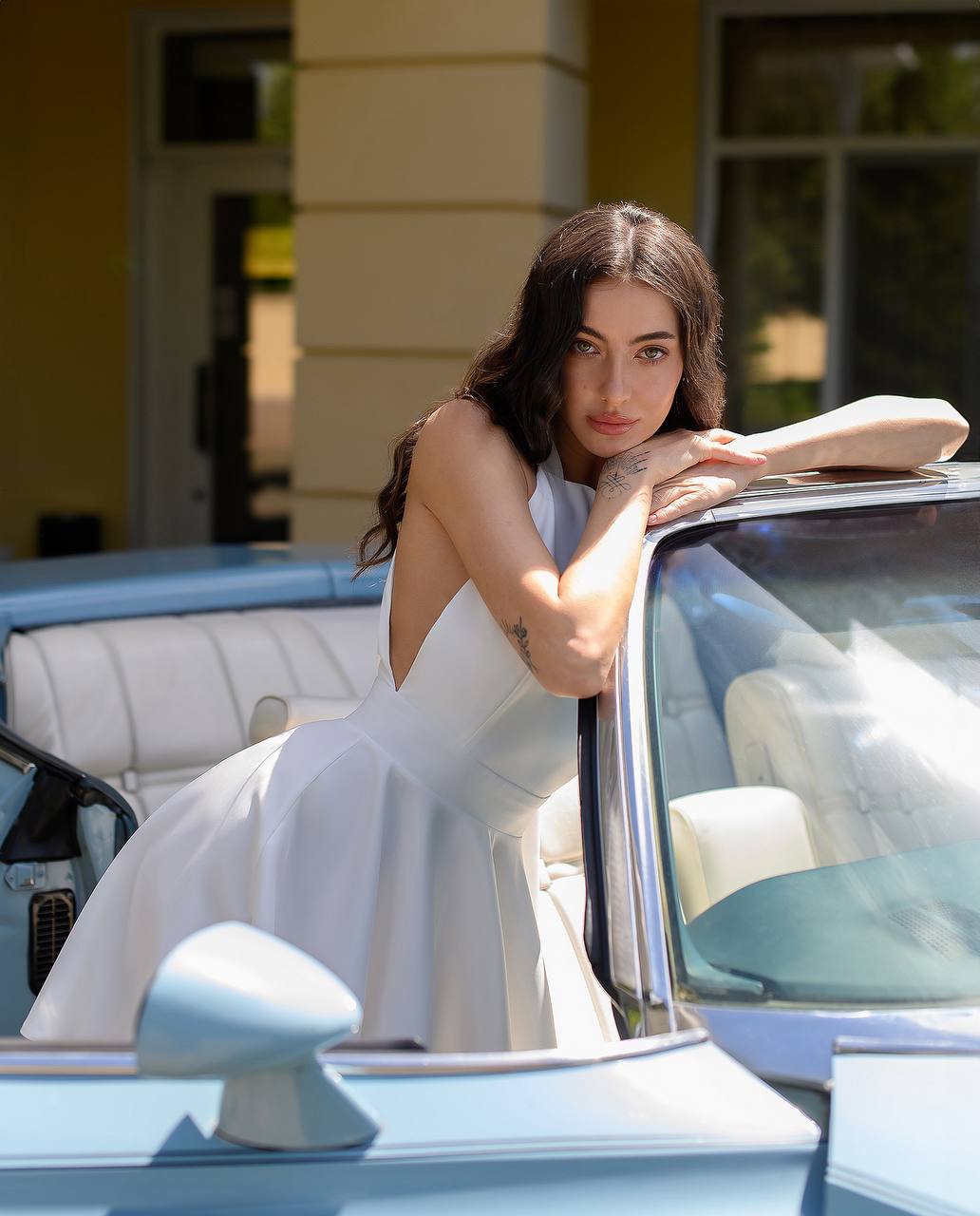 Woman in a white dress leaning on a vintage car outdoors