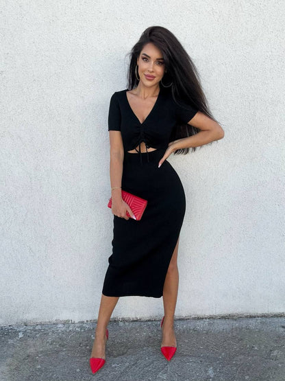 Woman in a black dress with a red clutch against a white wall