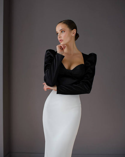 Woman wearing a black top and white pants against a gray background