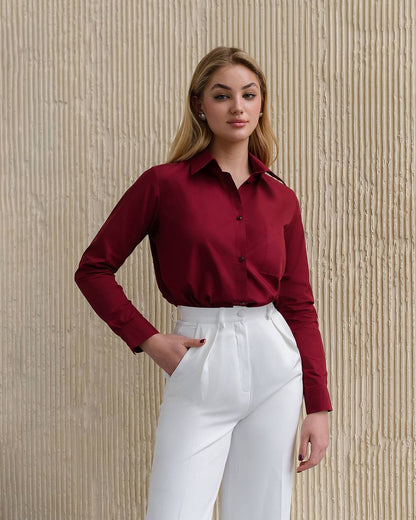 Woman wearing a red blouse and white pants against a beige textured wall