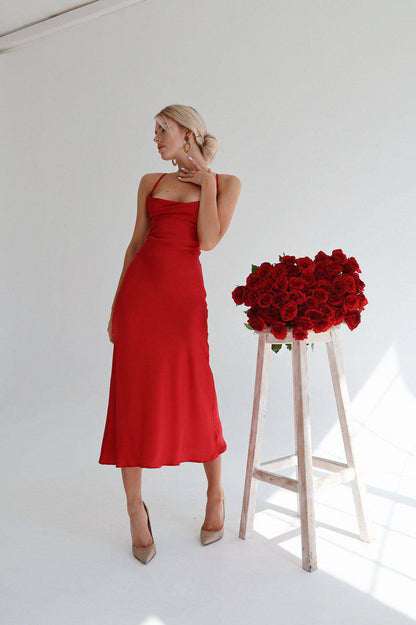 Woman in a red dress standing next to a stool with red roses against a white background