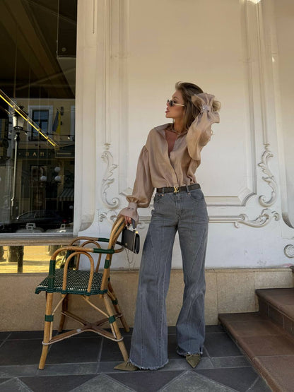 Woman in a beige blouse and blue jeans standing in front of an ornate building entrance.