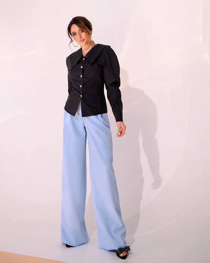 Woman wearing a black jacket and light blue pants against a white background