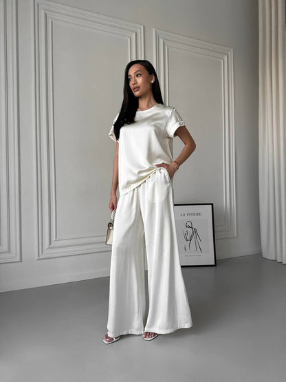 Woman in a white outfit standing in a minimalistic room with gray walls and a gray floor.