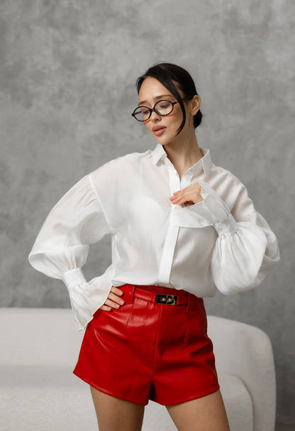 Woman wearing a white blouse and red shorts against a gray background