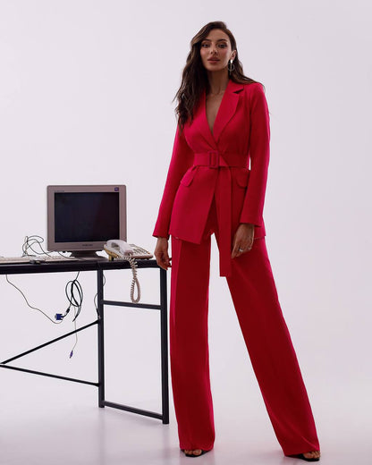 Woman in a red suit standing next to a desk with a computer and phone on a white background