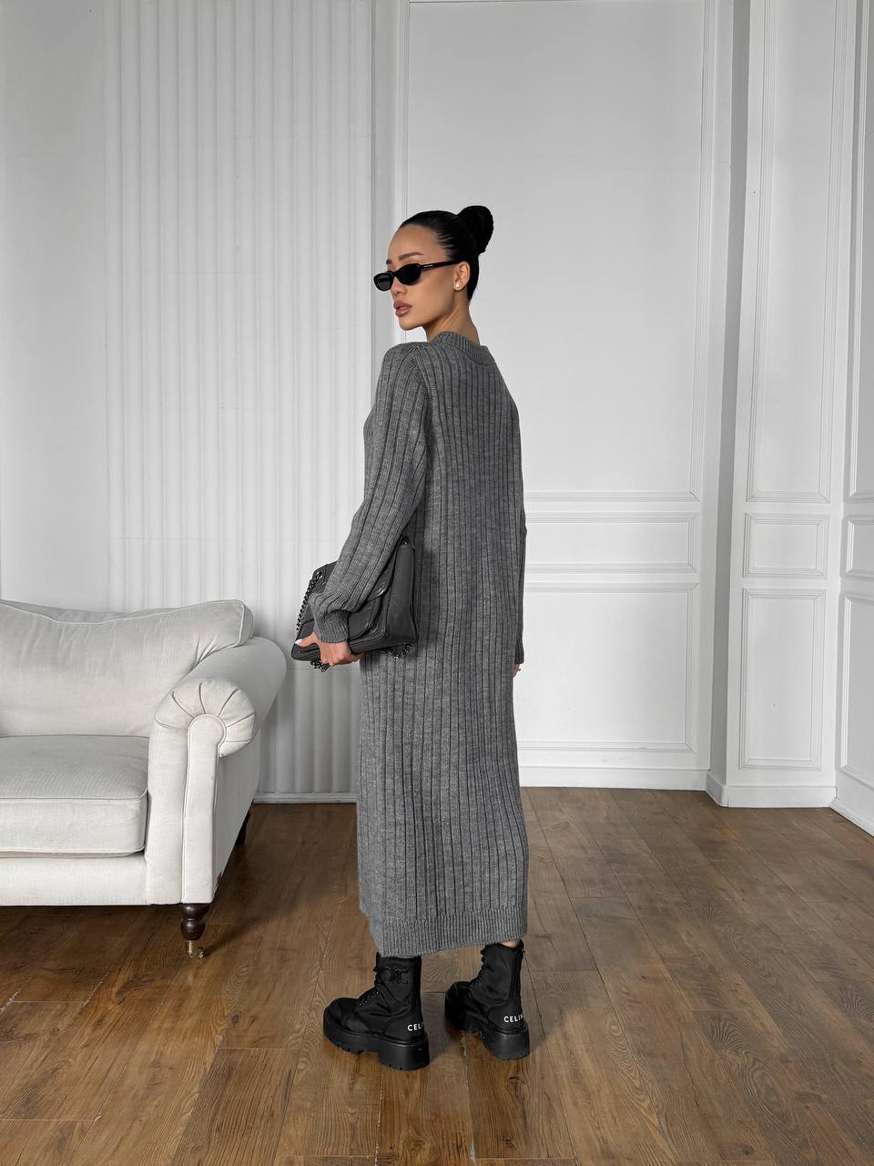 Person wearing a long gray ribbed sweater in a minimalistic room.