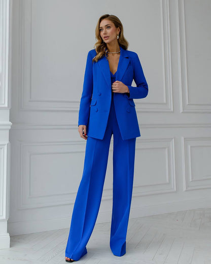 Woman wearing a blue suit standing against a white paneled wall.