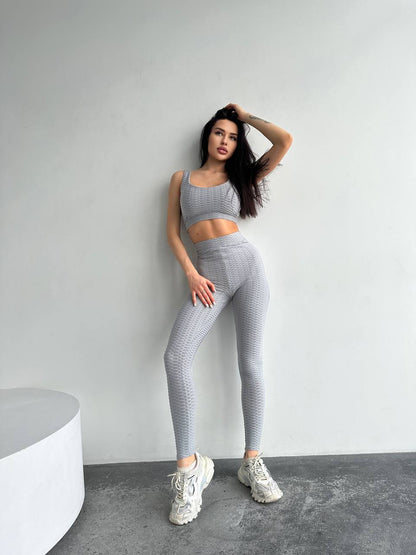 Woman wearing a gray athletic outfit posing against a plain background