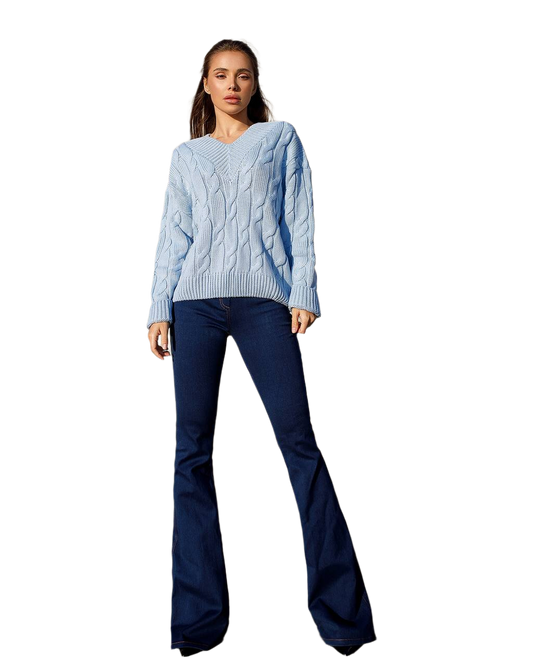 Woman wearing a light blue cable knit sweater and dark blue flared jeans on a white background
