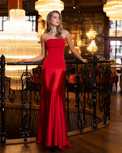 Woman in a red strapless gown standing in an elegant interior setting with chandeliers.