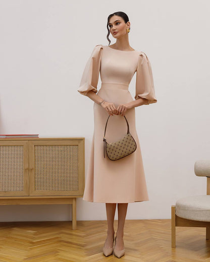 Woman in a beige dress holding a handbag in an indoor setting