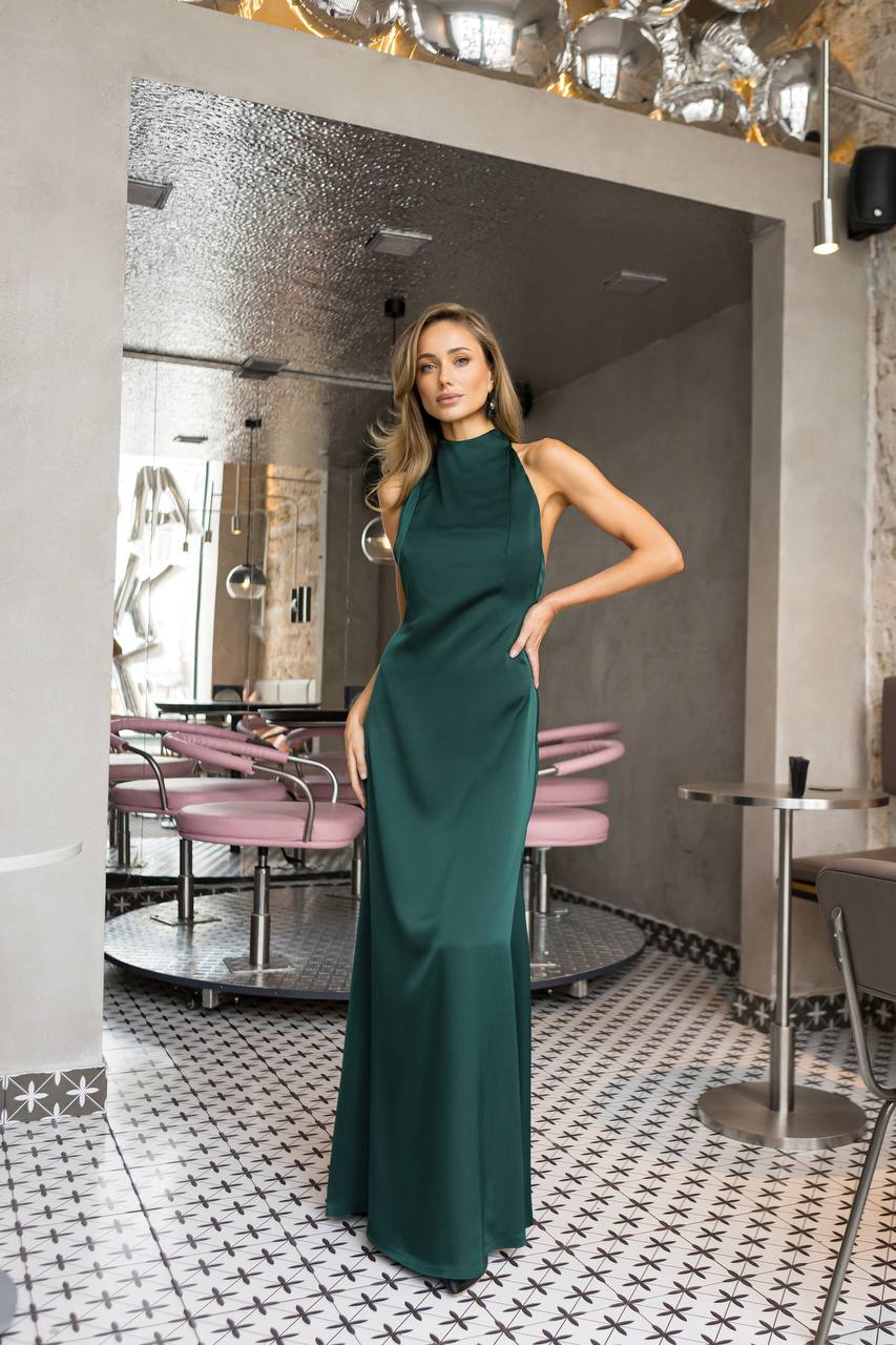 Woman in a green dress standing in a stylish interior setting with mirrors and tables.