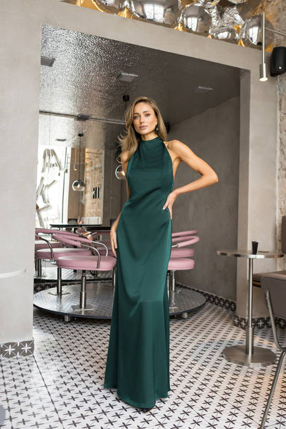 Woman in a green dress standing in a stylish interior setting with mirrors and tables.