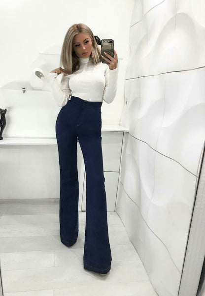 Person taking a mirror selfie wearing a white top and blue flared pants in a bathroom.