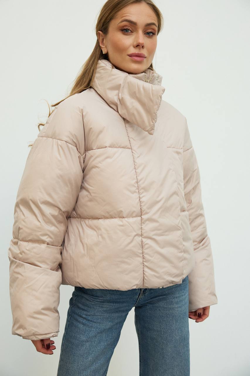 Woman wearing a beige puffer jacket against a white background