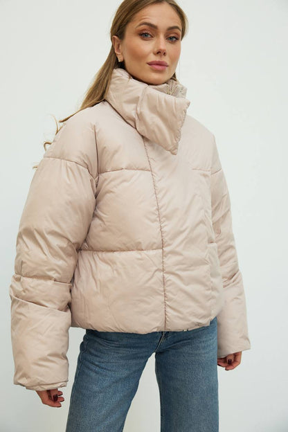 Woman wearing a beige puffer jacket against a white background