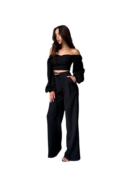 Woman wearing a black off-shoulder top and wide-leg pants on a white background