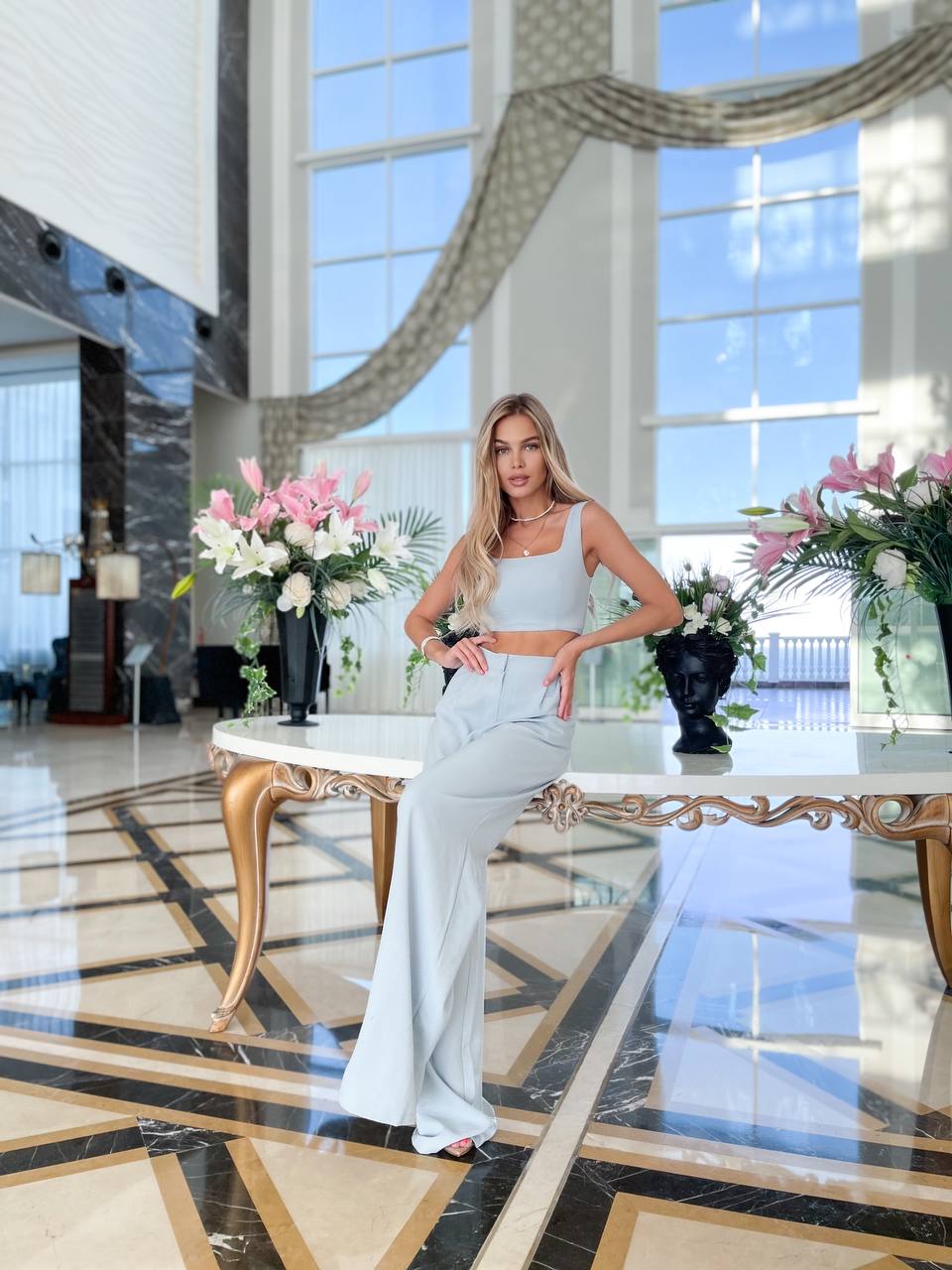 Woman in a white dress standing in a luxurious interior setting with large windows and marble floor.