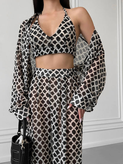 Woman wearing a patterned outfit with a black handbag against a white wall.