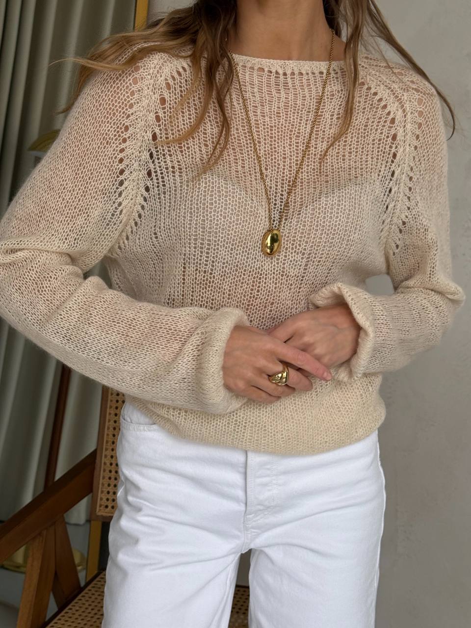 Person wearing a beige knit sweater and white pants indoors.