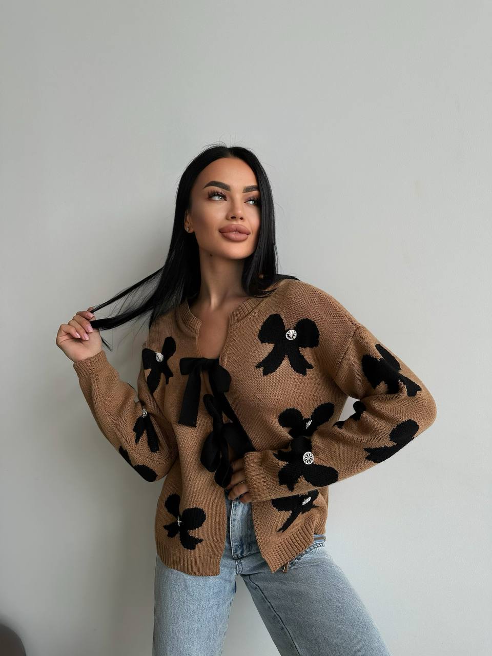 Woman wearing a brown sweater with black floral patterns against a plain background