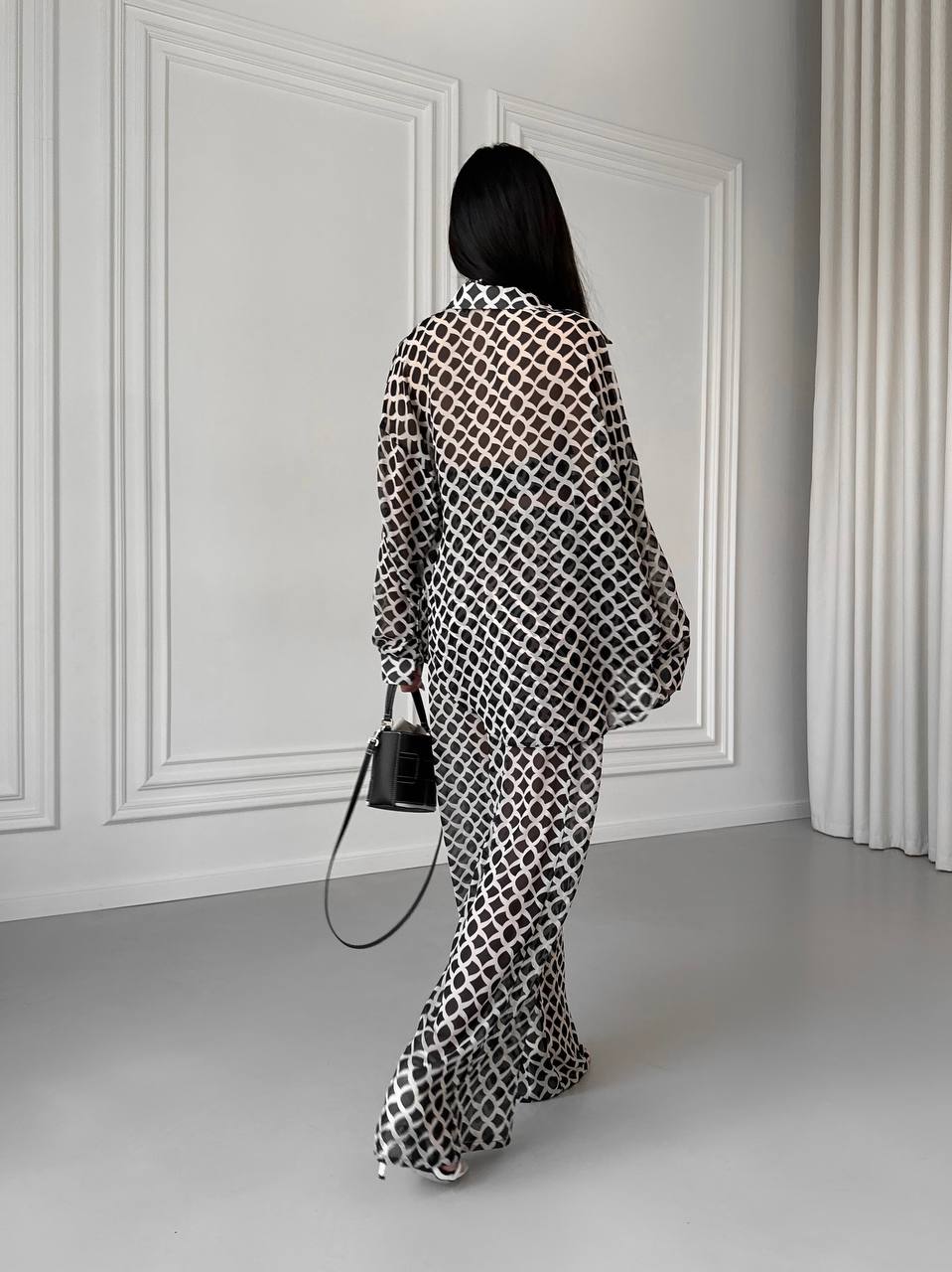 Person wearing a patterned outfit standing in a room with white walls and gray floor.