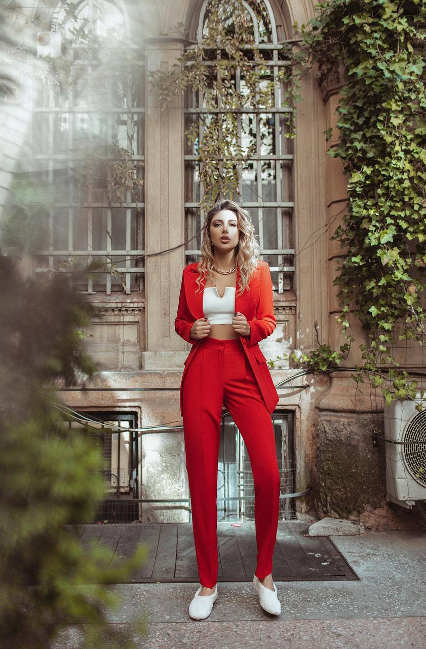Woman in a red suit standing in front of an architectural building with greenery.