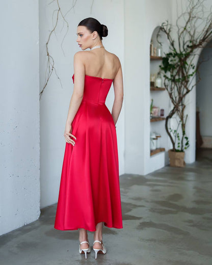 Woman in a red strapless dress standing in a room with white walls and a plant.