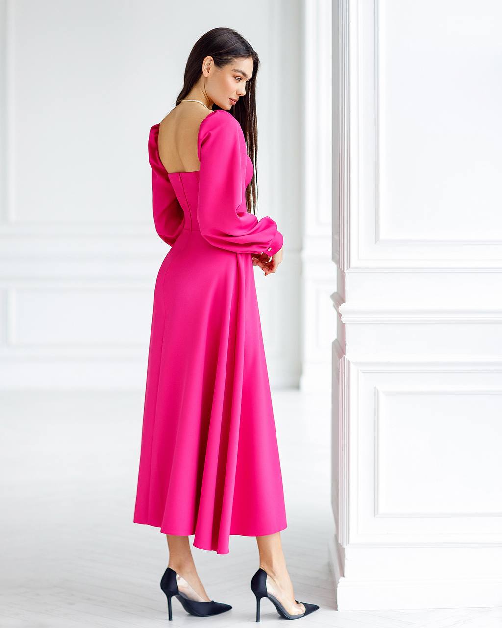 Woman wearing a bright pink dress with long sleeves in a minimalistic setting.