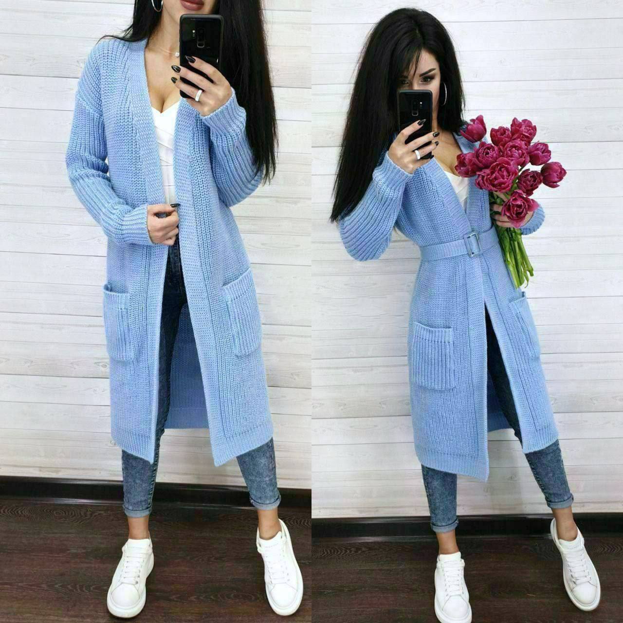 Woman wearing a long blue cardigan holding flowers indoors.