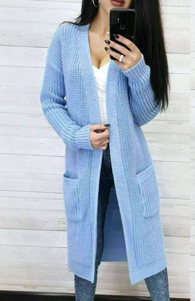 Person wearing a light blue knitted cardigan against a white wooden panel background