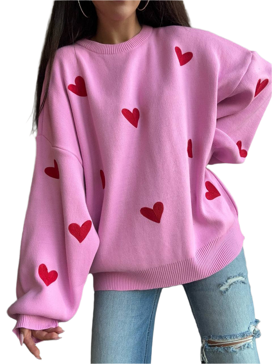 Pink sweater with red heart patterns worn by a person on a white background