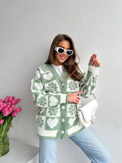 Woman wearing a green and white patterned cardigan with a vase of pink tulips in the background.