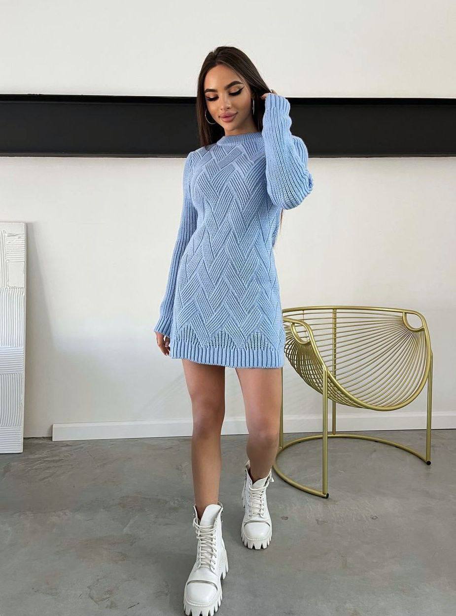 Woman wearing a light blue knitted dress with white boots in a minimalistic room.