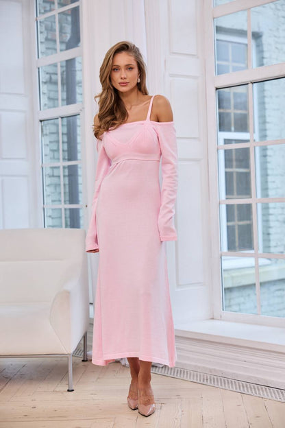 Woman wearing a pink dress standing in a bright room with large windows.